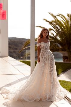 a woman in a wedding dress is standing on the porch with palm trees behind her