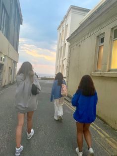 three girls are walking down the street in front of some buildings and one girl is wearing white shoes