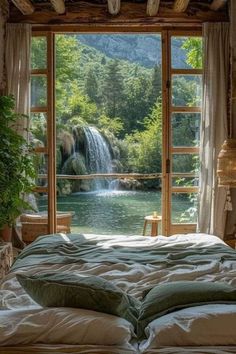 there is a bed with pillows on it in front of a window that looks out to a waterfall