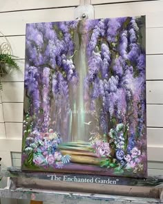 an easel with a painting on it and purple flowers in front of the frame