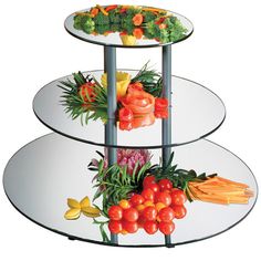 three tiered glass plate display with fruits and vegetables on each side, in front of a white background