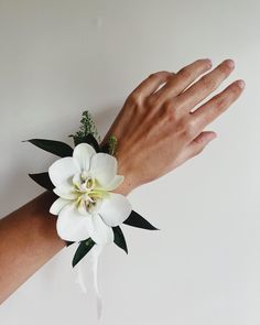 a person's hand with a wrist corsage and white flowers on it