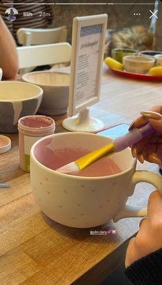 a person is mixing something in a bowl with a yellow marker on it while another person sits at the table