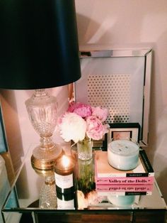 a glass table topped with books and vases next to a lamp on top of it