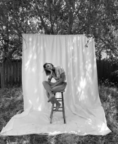 a black and white photo of a woman sitting on a stool in front of a backdrop