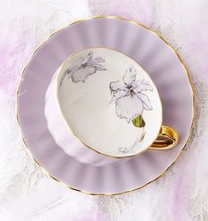 a cup and saucer with flowers painted on the side, sitting on a feathery surface