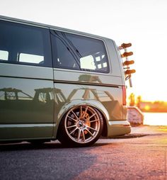 a green van parked in front of a body of water with the sun setting behind it