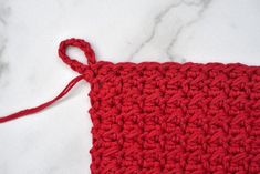 a red crochet square is shown on a white marble surface with a string attached to it