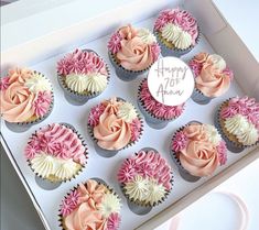 twelve cupcakes with pink and white frosting in a box on a table