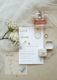 wedding stationery with rings, ring box and flowers on the bed sheet next to it