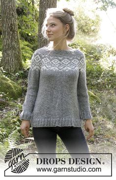 a woman standing in the woods wearing a sweater