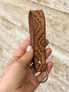 a hand holding a brown leather keychain with an arrow design on it's side