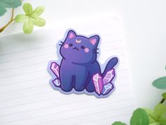 a purple cat sticker sitting on top of a notepad next to a plant