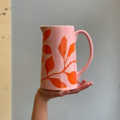 a hand holding a pink coffee mug with orange leaves painted on the outside and inside