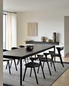 a dining room table with chairs and a bowl on it in front of a window