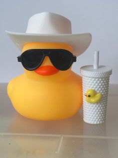 a rubber duck wearing sunglasses and a white cowboy hat next to a drink in a plastic cup