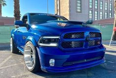 a blue truck parked in a parking lot next to a tall building with palm trees