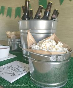 a bucket full of popcorn and bottles of beer on top of a green tablecloth