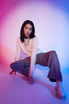 a woman sitting on top of a chair in front of a pink and blue background