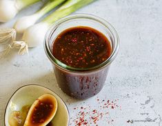 a jar of sauce next to two spoons on a plate with onions and garlic