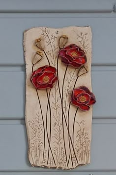 an art piece with three red flowers on the side of a house door, painted in white and brown