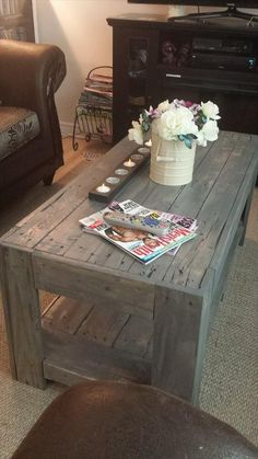 a coffee table with magazines and flowers on it in front of a television set,