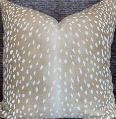 a brown and white pillow sitting on top of a wooden table next to a brick wall