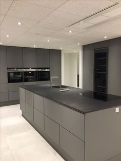 an empty kitchen with grey cabinets and black counter tops, lights on above the sink