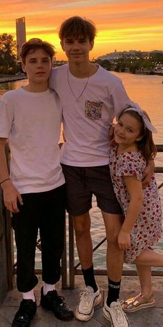 two boys and a girl standing on a pier at sunset