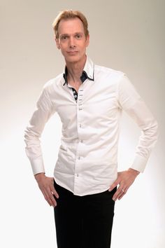 a man in white shirt and black pants standing with his hands on his hips while looking at the camera