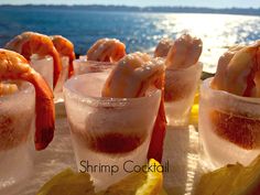 several glasses filled with ice and shrimp on top of a table next to the ocean