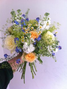 a person holding a bouquet of flowers in their hand with white and blue flowers on it