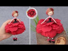 a hand holding a red doll on top of a piece of wood next to a flower