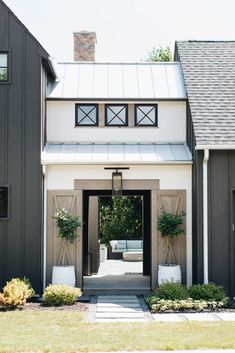 the front entrance to a house with two white chairs and potted plants on either side