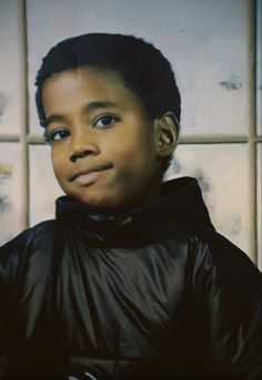 a young boy wearing a black jacket in front of a tiled wall