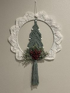 a crocheted christmas ornament hanging on the wall with berries and greenery