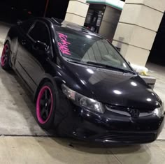 a black car with pink rims parked in front of a building