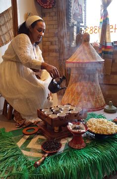 a woman in white dress pouring tea on top of a green table covered with food