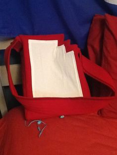 a red bag sitting on top of a bed next to a blue and white blanket