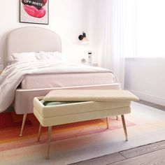 a white bed sitting next to a blue ottoman on top of a wooden floor in a bedroom