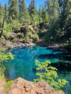 the blue lake is surrounded by pine trees and rocks, with clear water running through it