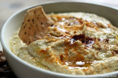 a white bowl filled with hummus and a tortilla chip