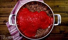 a pot filled with meat and sauce on top of a wooden table