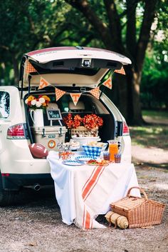 an open trunk of a car with food and drinks on the table next to it