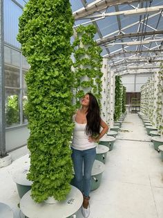 a woman standing next to a tall plant in a greenhouse