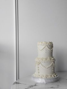 a three tiered white wedding cake sitting on top of a marble counter next to a silver pole