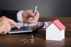 a person using a calculator, pen and paper house next to keys on a desk