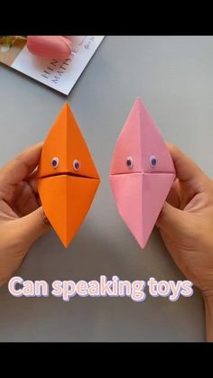 two hands holding origami birds with eyes and mouths, one is orange and the other is pink