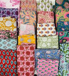 many different colored and patterned fabrics are stacked up on each other in rows, with one folded over the top