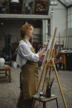 a woman standing in front of an easel holding a paintbrush